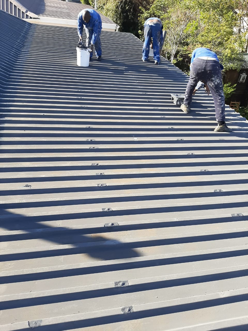 Three of the crew working their way up a sheet roof with coating and brushes