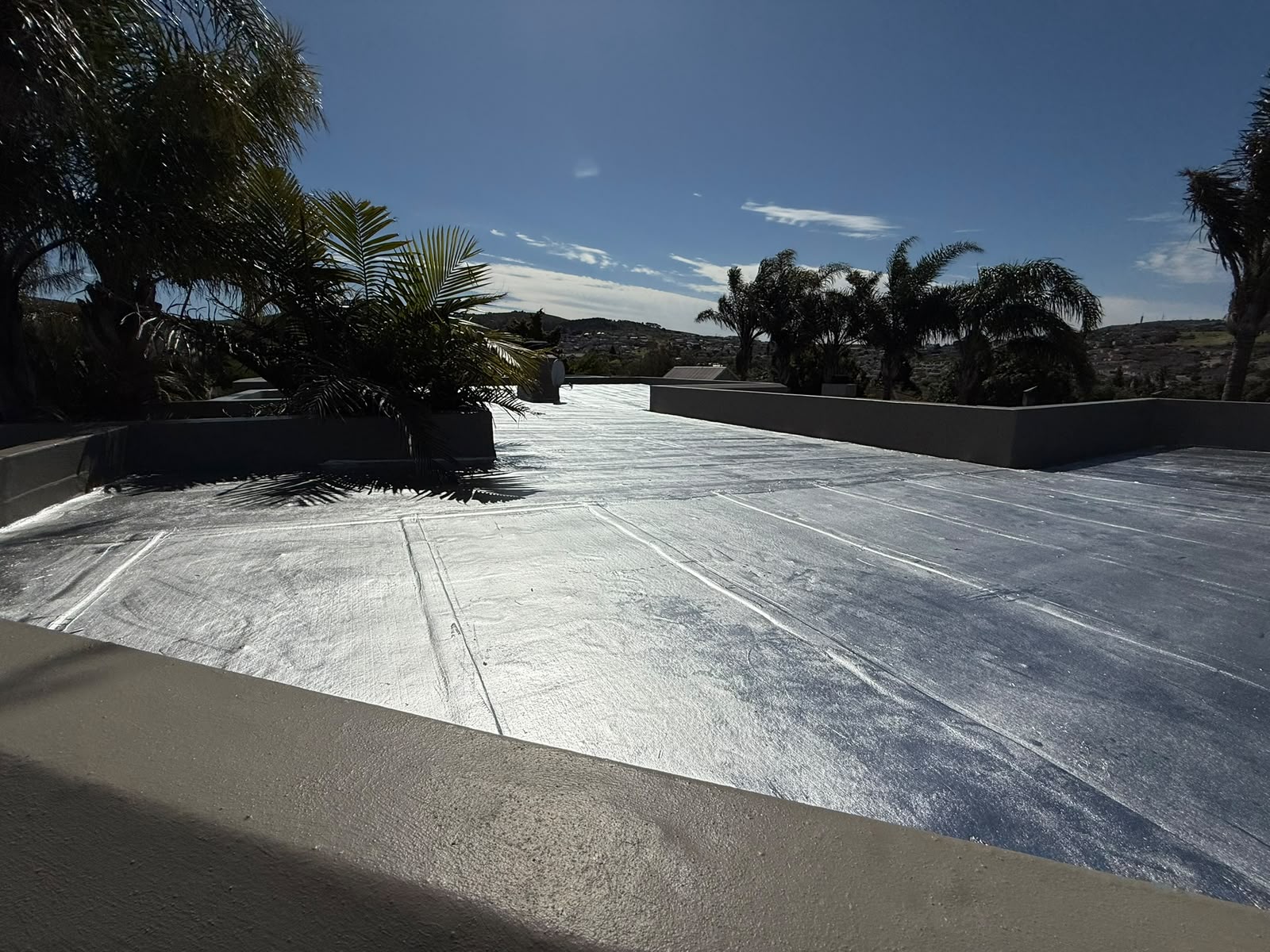 Flat roof finished in a reflective aluminium coating, turned up into the parapets