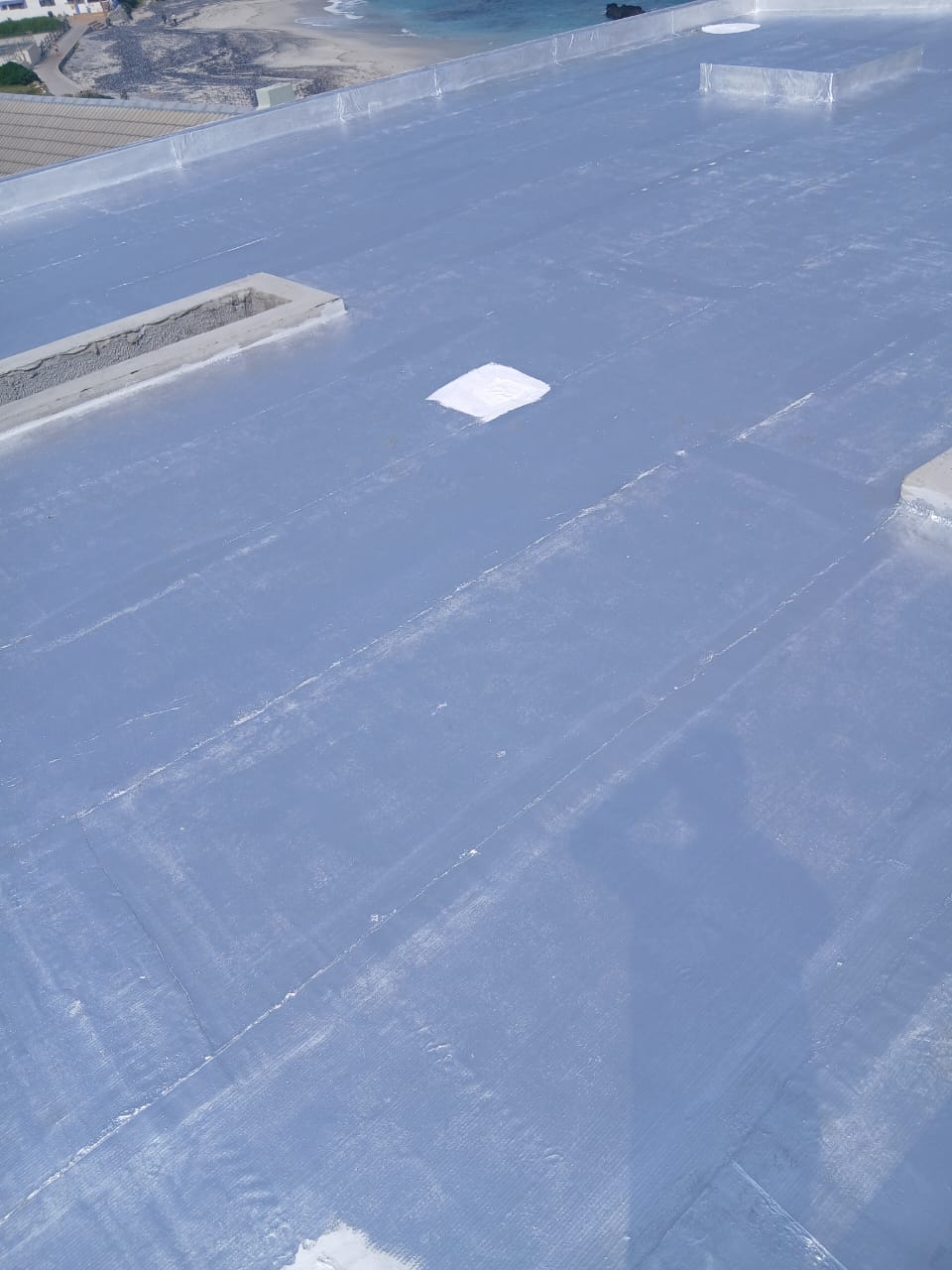 Finished pale grey membrane across a large flat roof, turned up into the parapets and dressed around the penetrations