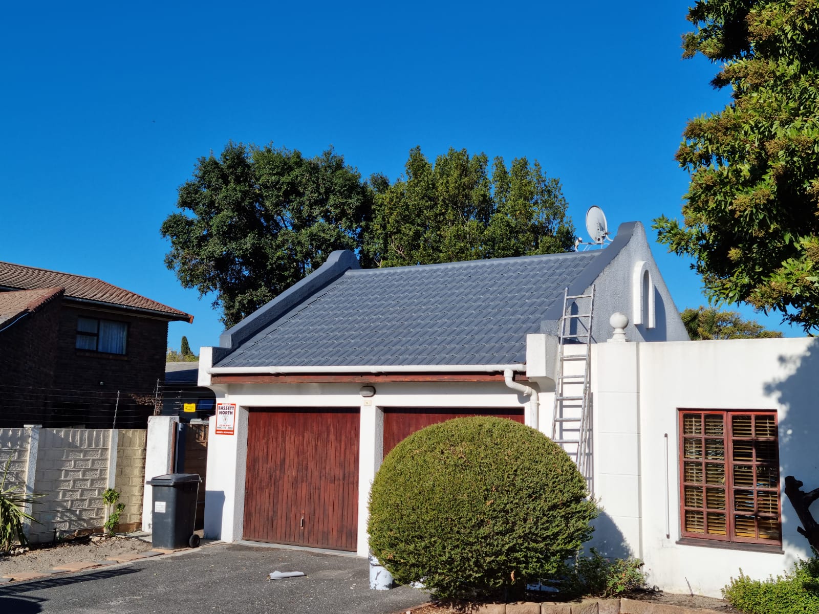 Whole house with its tiled roof freshly coated, ladder still against the gable