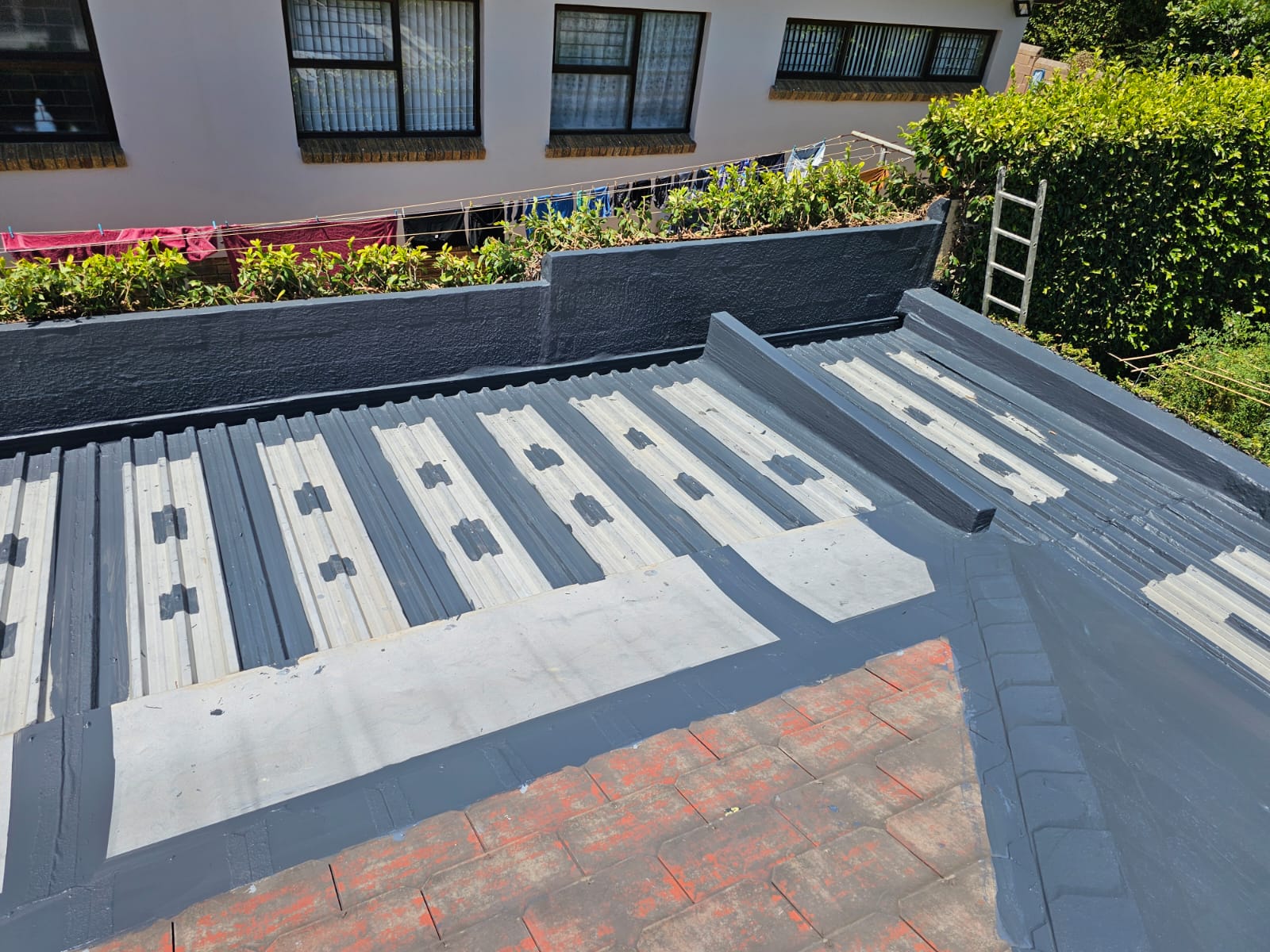 Corrugated metal roof coated in grey, with reinforcing strips bedded over every fixing line