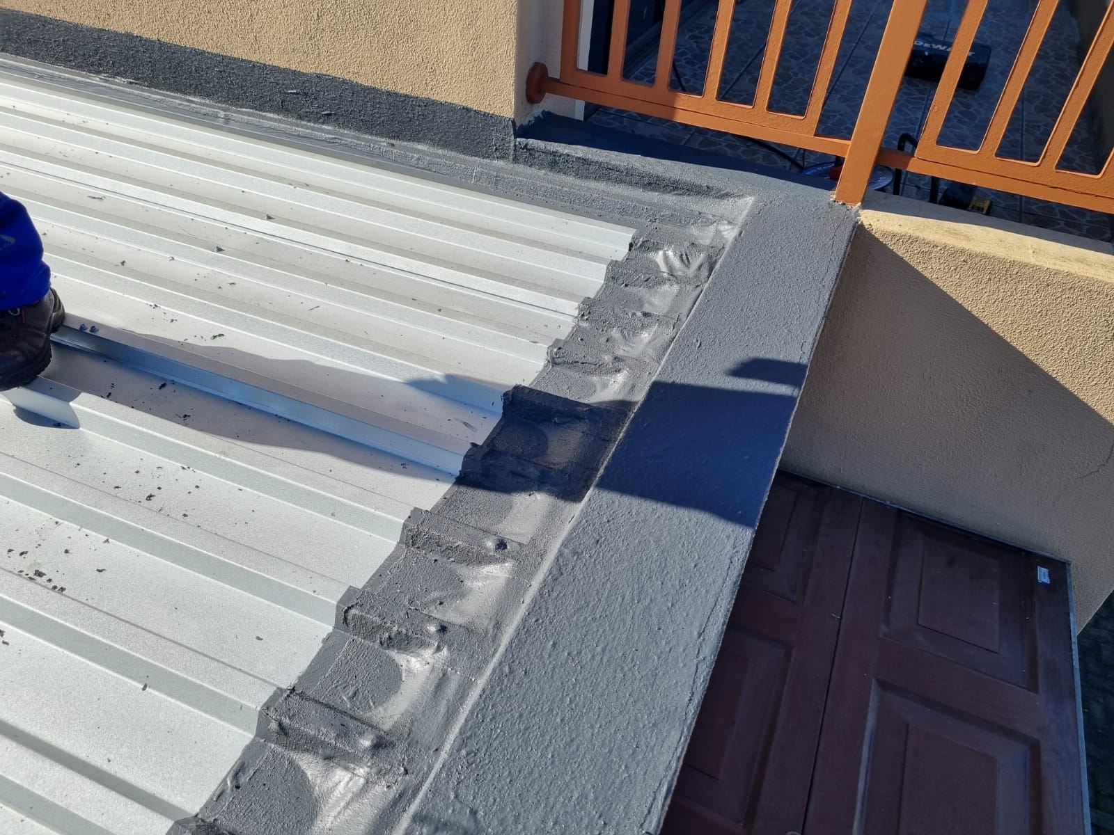 Flashing detail where a sheet roof meets a parapet wall, sealed and coated