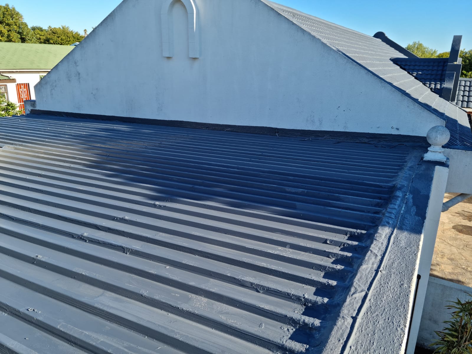 Coated sheet roof running into a rendered gable, with the joint sealed