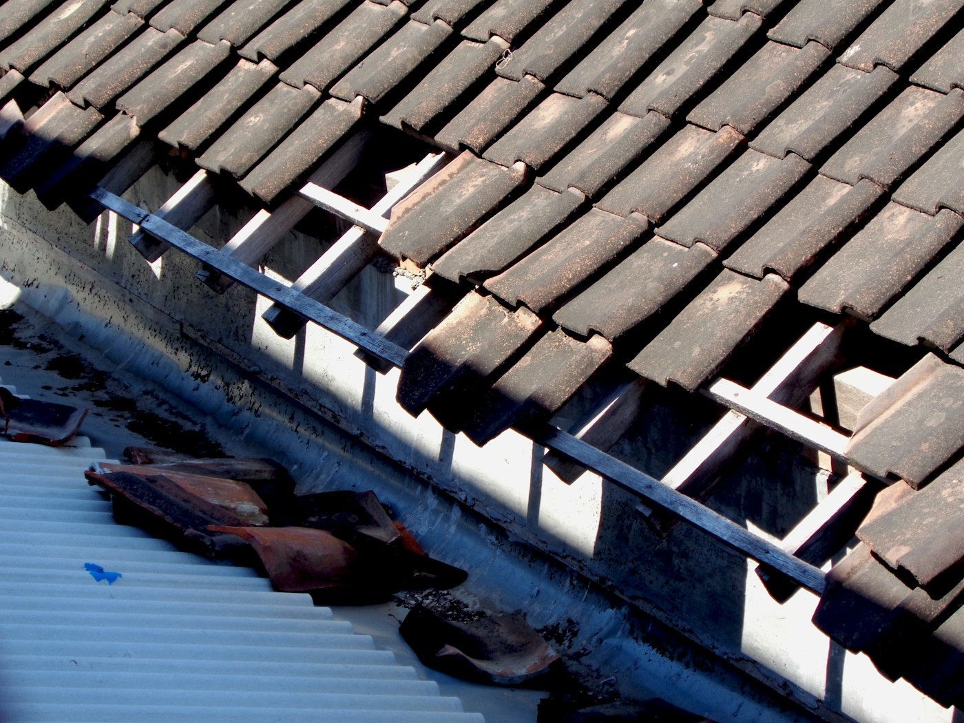 Debris and broken tile collecting in a gutter under the edge of a tiled roof